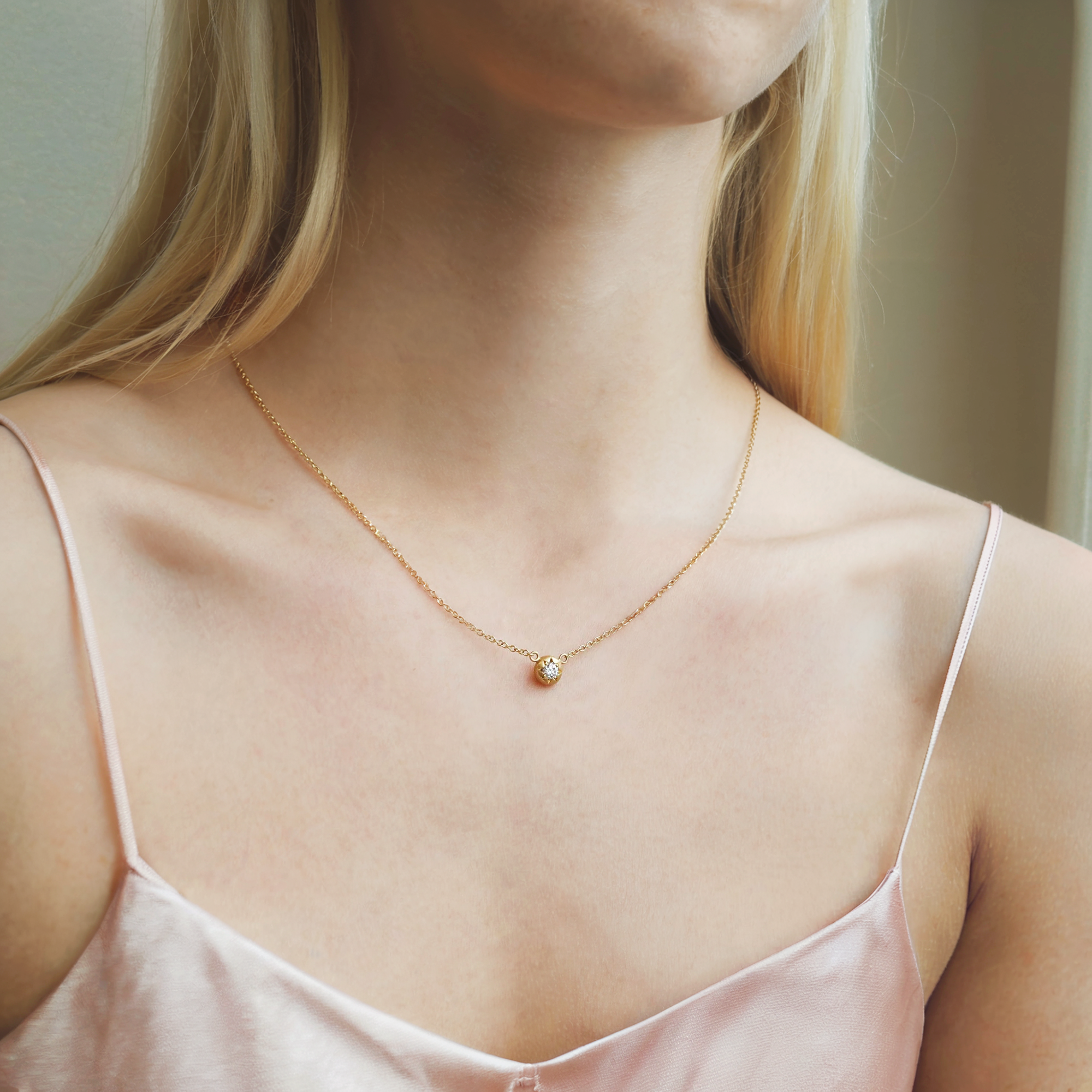 A collection of dainty 14k solid gold minimalist necklaces displayed on a neutral background, featuring fine chains and small charms ideal for layering.