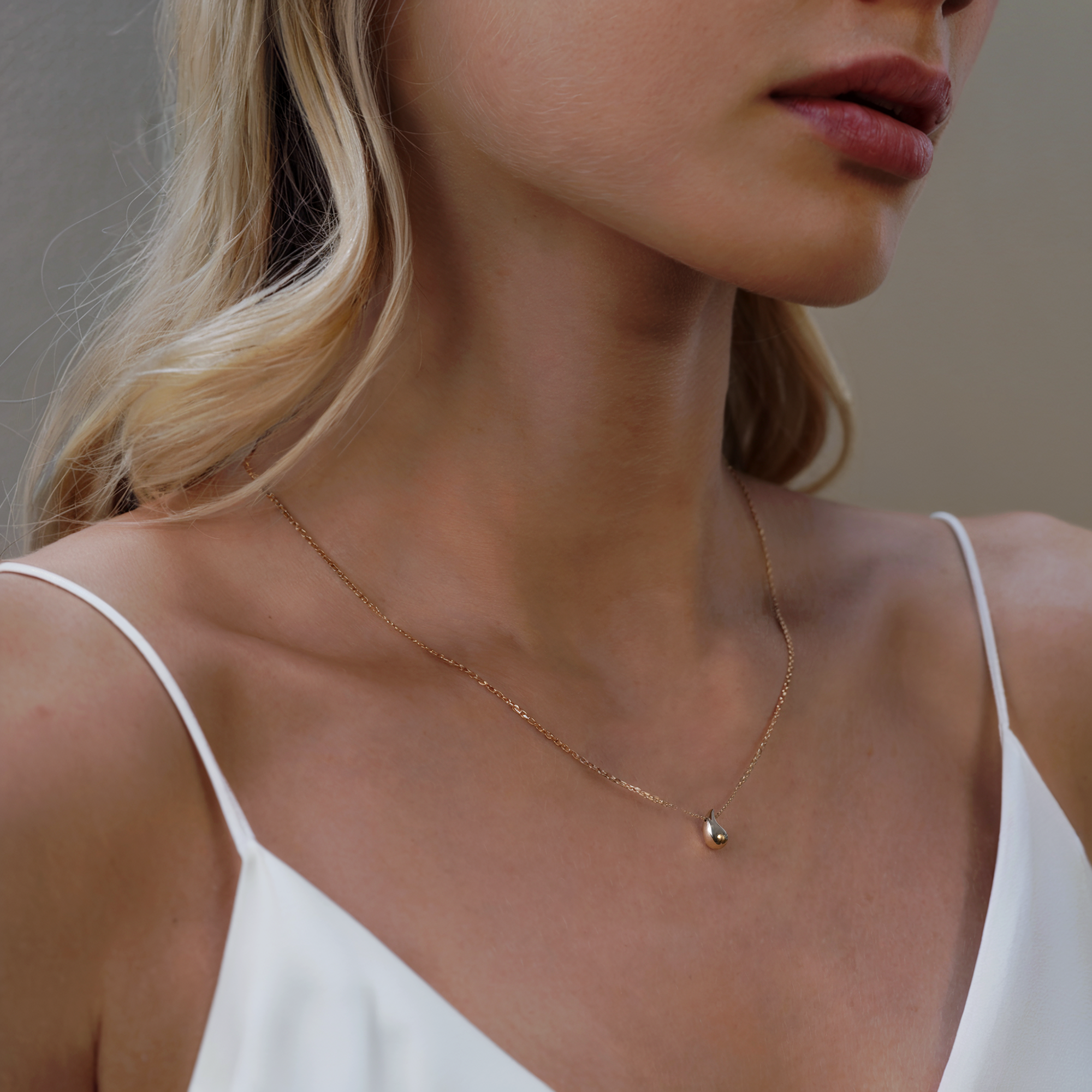 Close-up of a woman wearing a delicate gold necklace against a neutral background