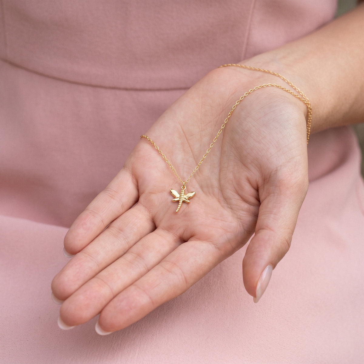 Winged pendant held in an open hand, its fine chain falling across the palm