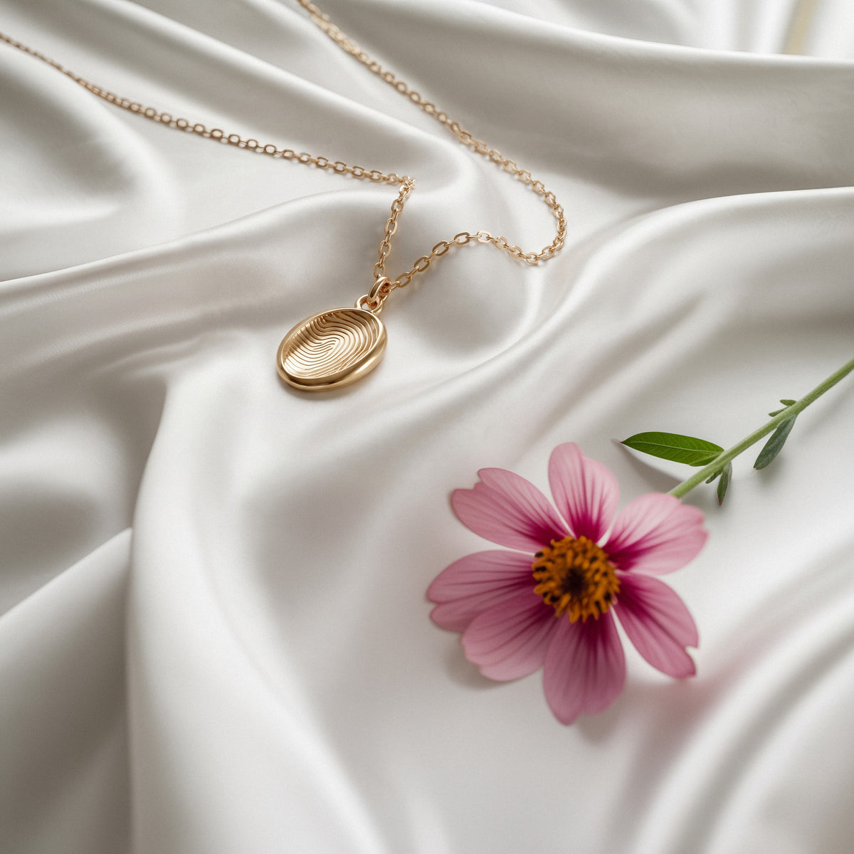 Fingerprint pendant on ivory silk with a pink cosmos flower, engraved surface facing the light