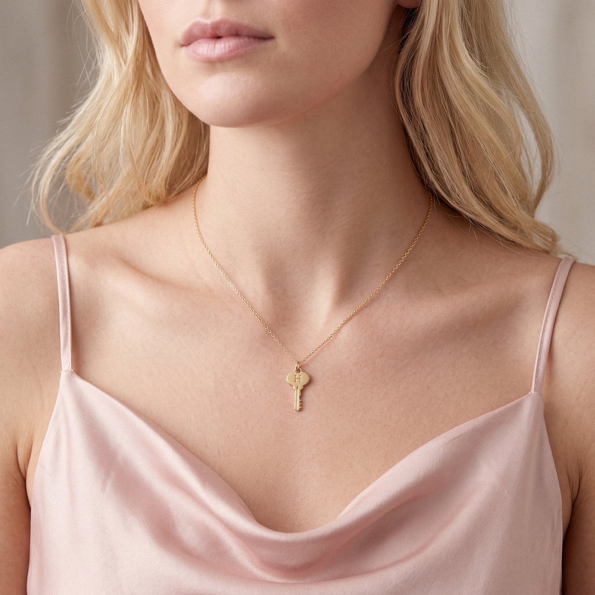 Gold key pendant sitting just below the collarbone on a model in a rose toned camisole