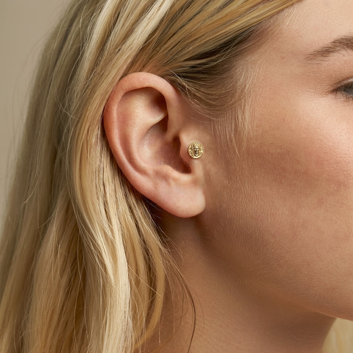 Close ear view of the Medusa portrait flatback piercing, revealing its compact mythological profile in a curated stack.
