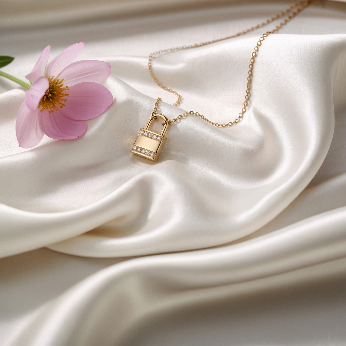 Gold padlock diamond necklace resting on ivory silk next to a lilac flower