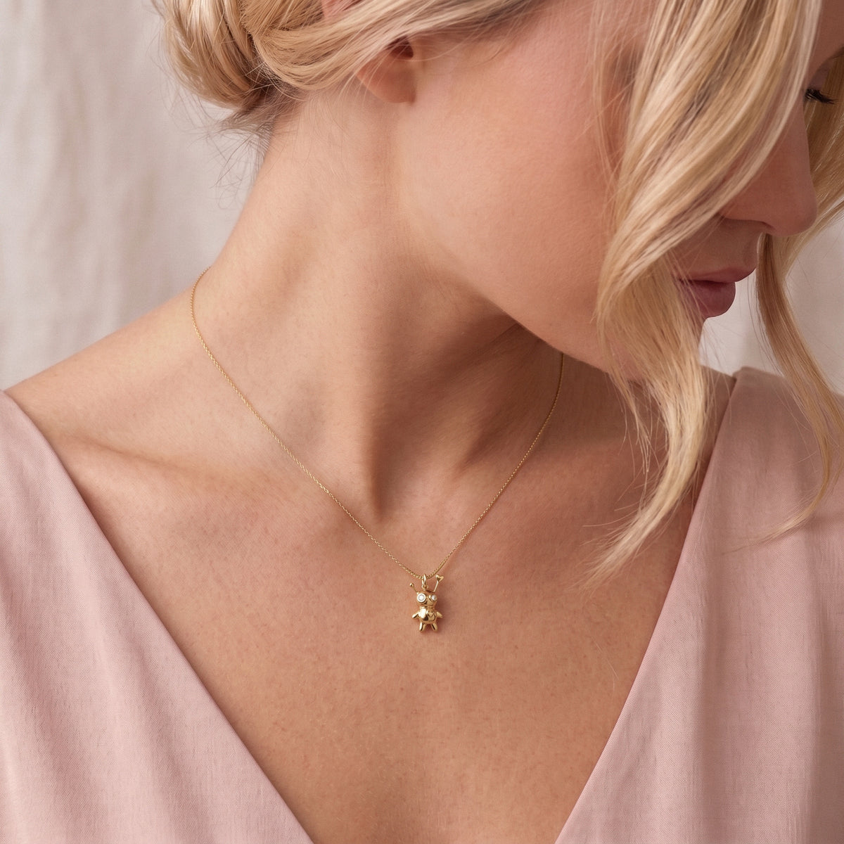 Voodoo doll necklace worn with a deep pink v-neck, charm resting below the collarbone