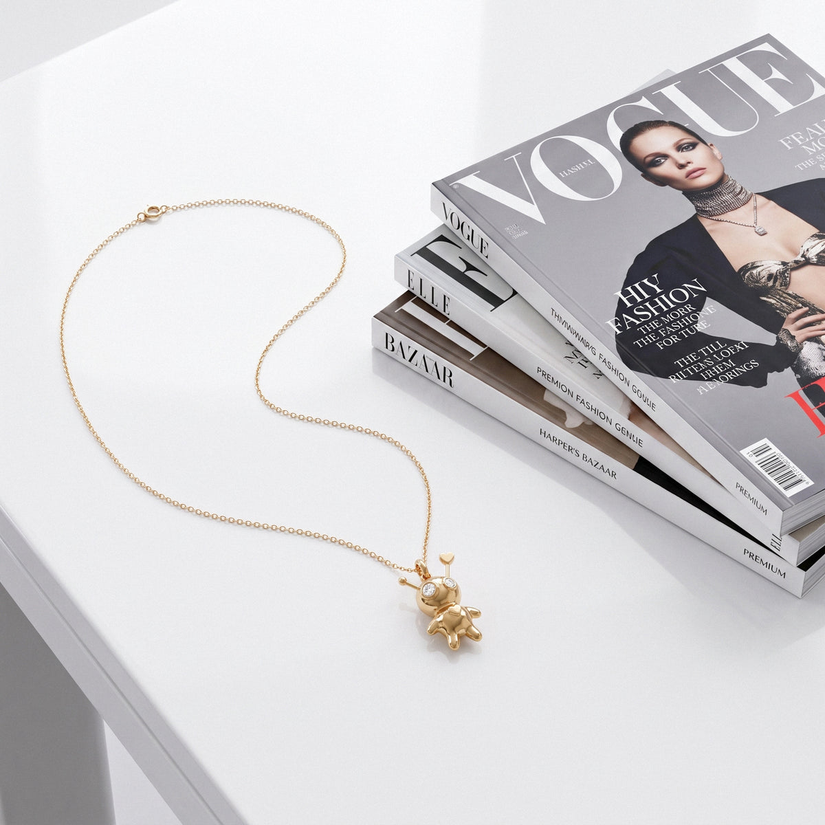 Doll pendant necklace laid out on Vogue and Bazaar magazines on a white table