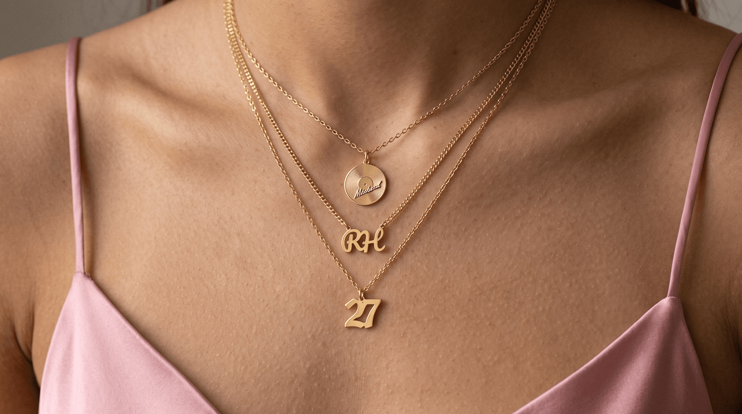 Personalized 14K gold initial pendant necklace and name necklace layered on a neutral linen surface