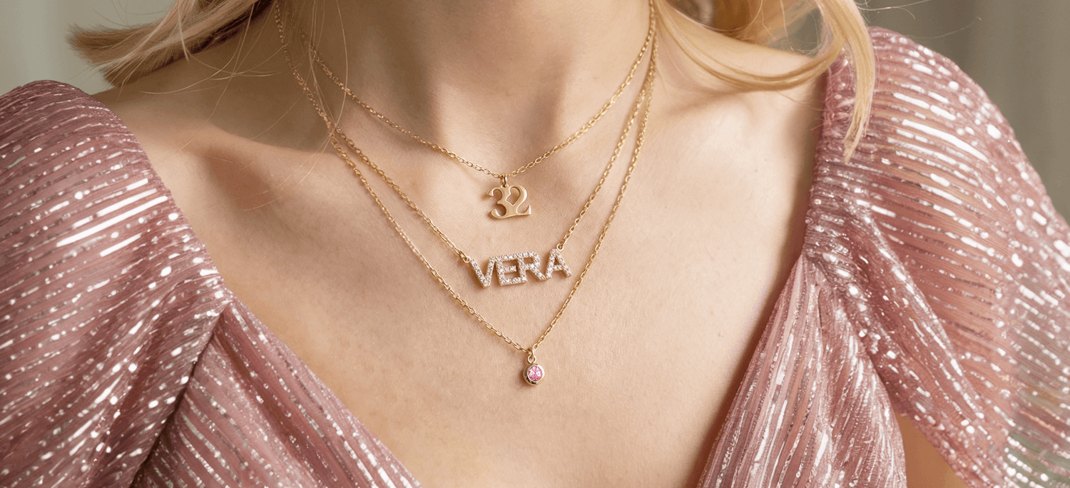 Custom 14K gold personalized jewelry including name necklaces, initial charms, and engraved tags displayed on soft fabric.