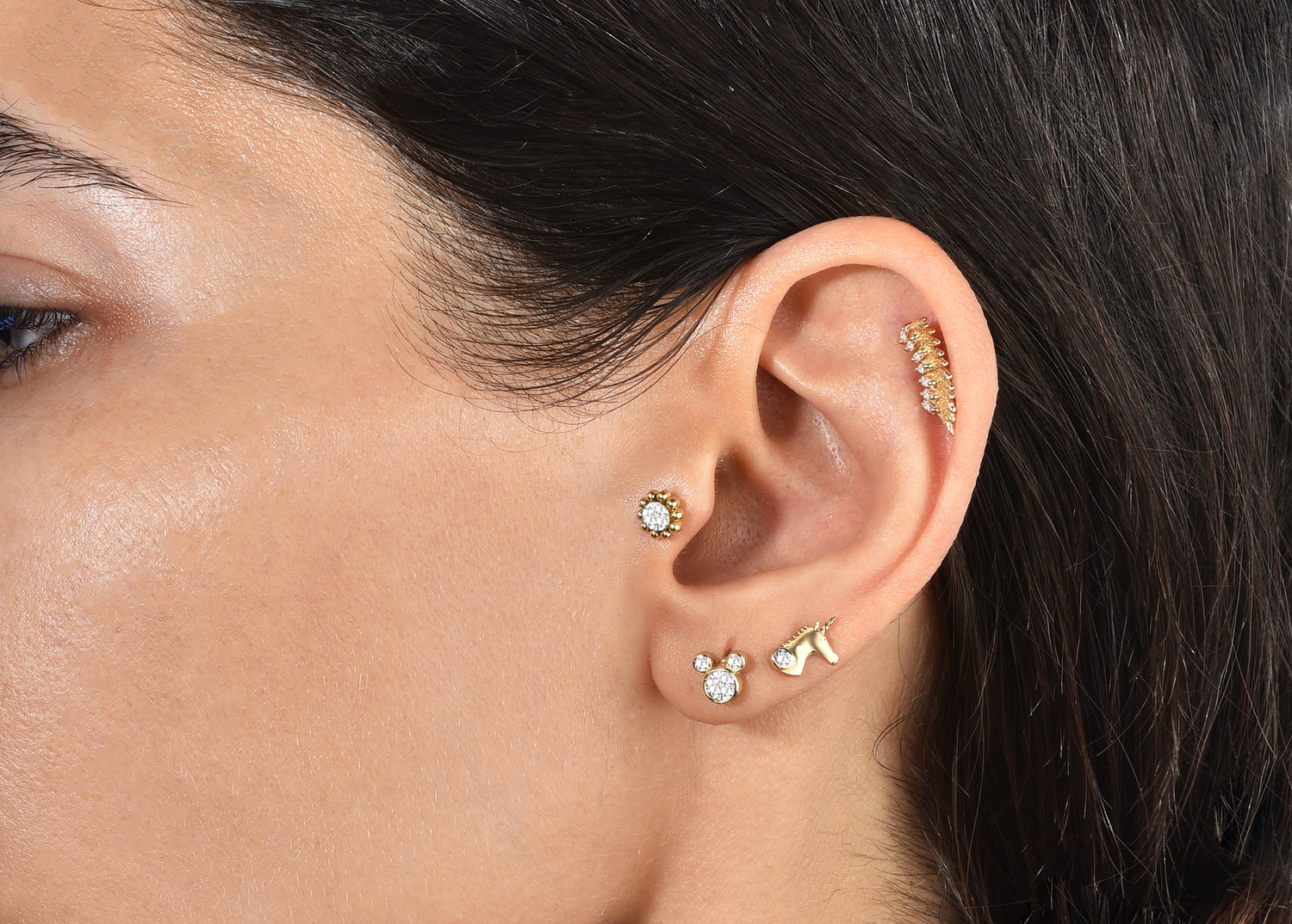 lose-up of a curated ear stack featuring 14K solid gold diamond stud piercings in the helix and tragus, and marquise-cut diamond hoops on the lobe.