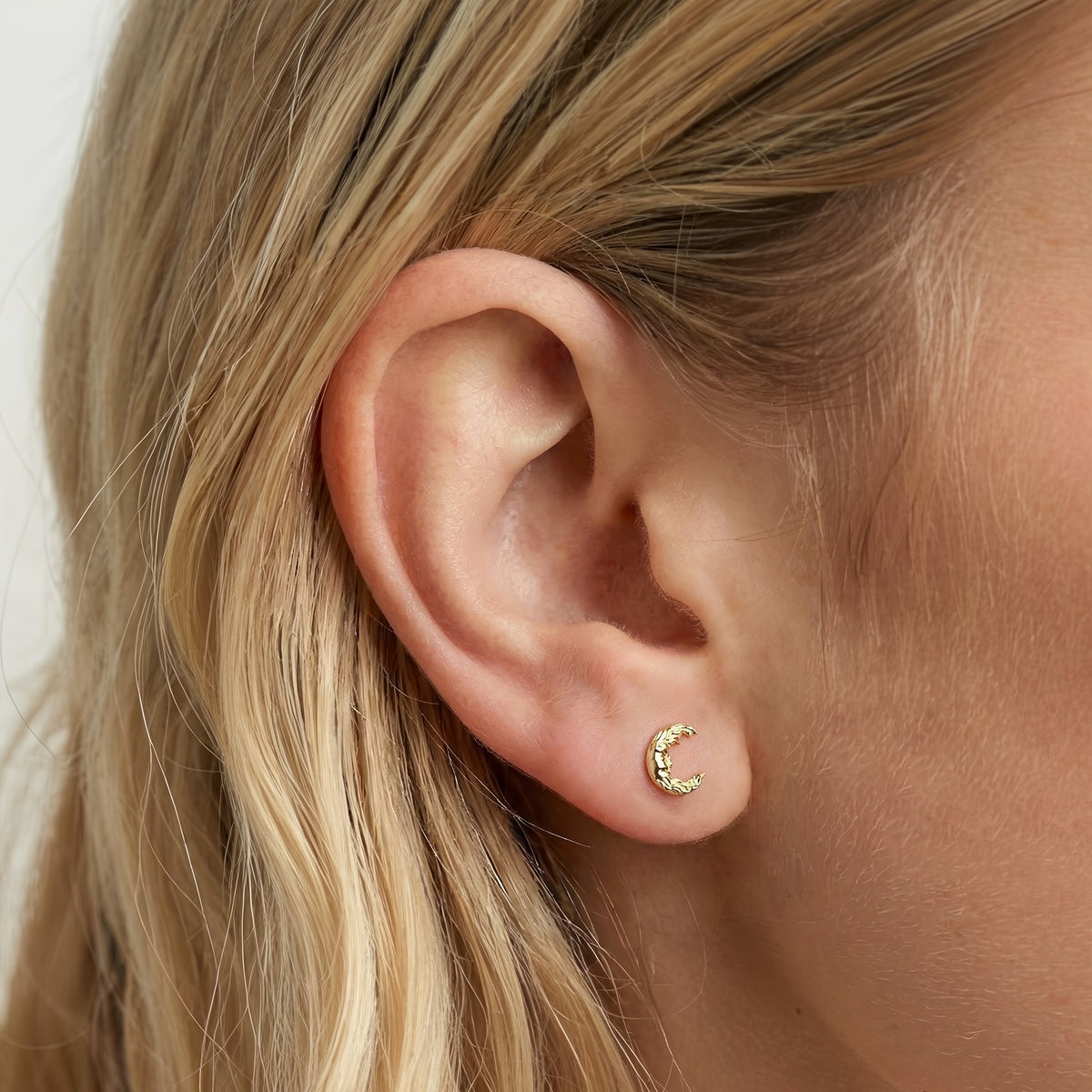 Close earlobe view of an open crescent moon face earring catching warm light