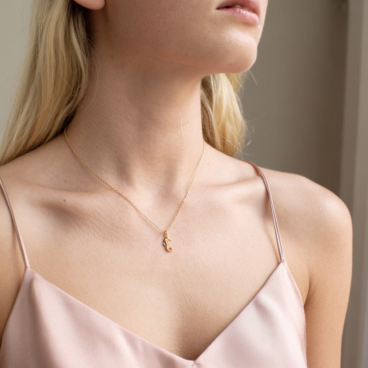 Close crop of the seahorse charm on a model in a blush strap dress