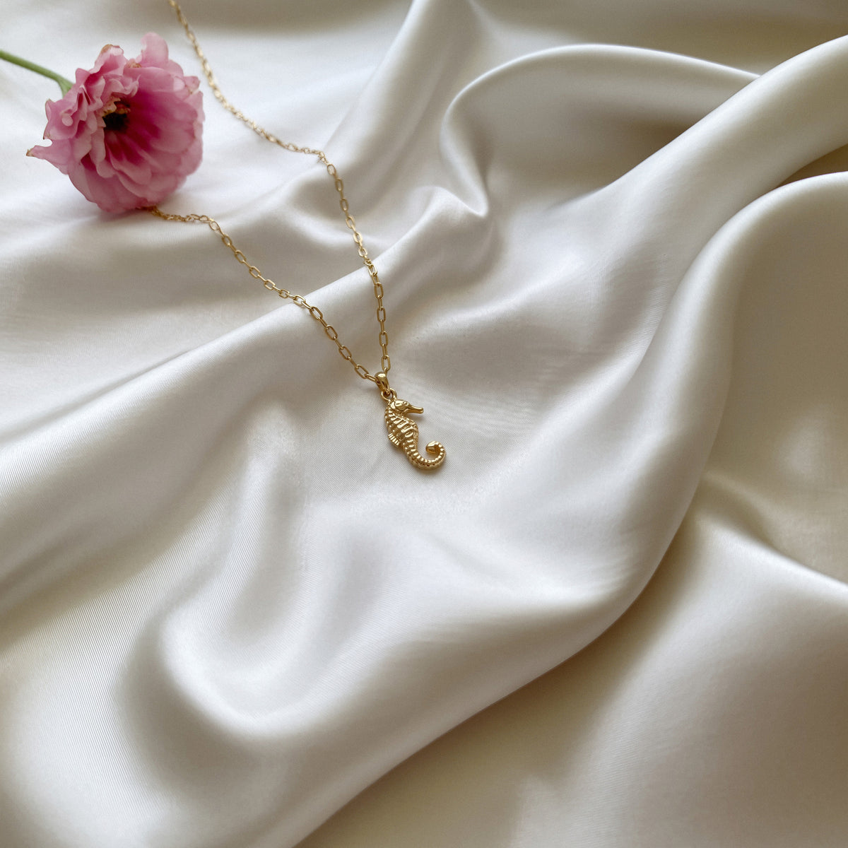 Seahorse pendant on rippled white silk beside a pink tulip