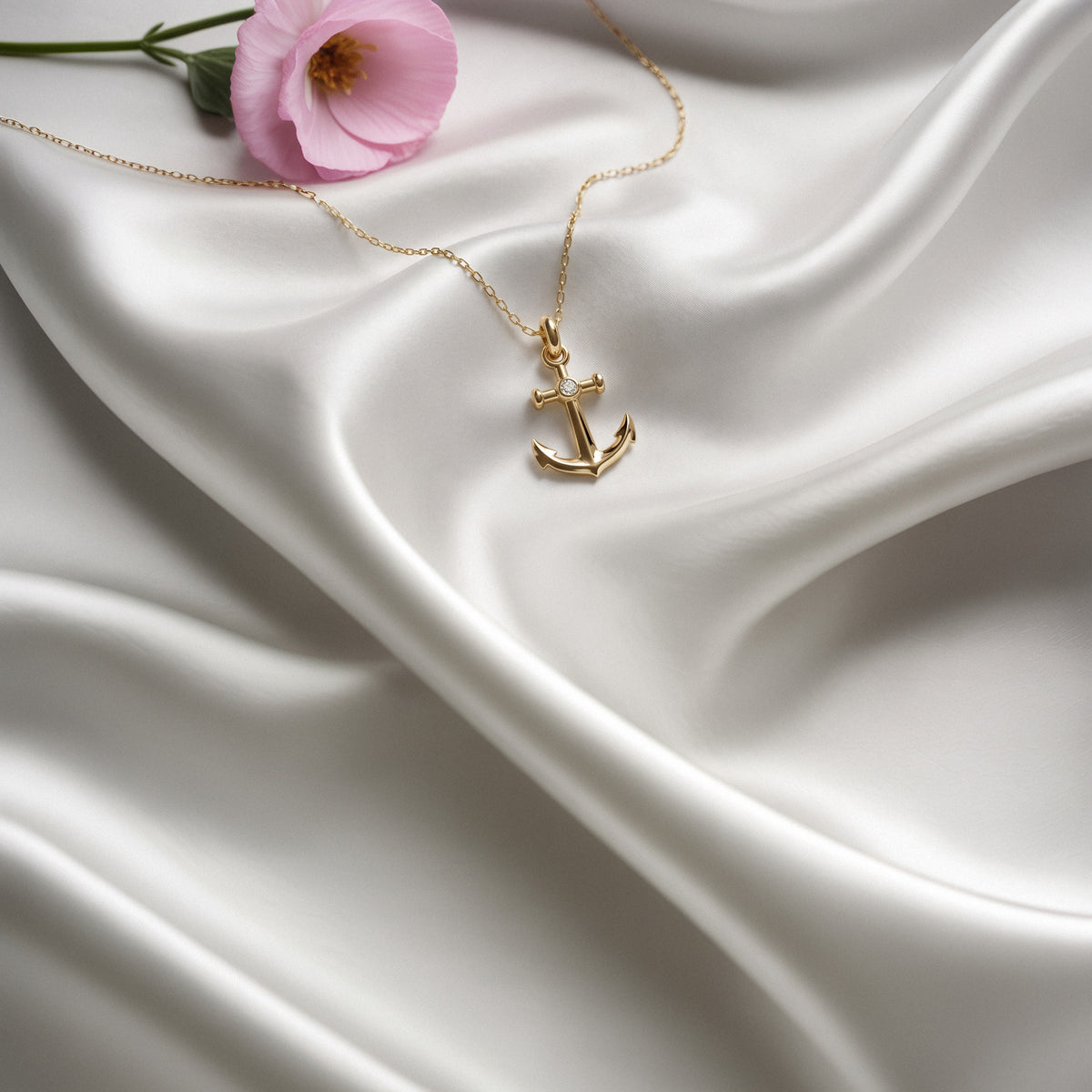 Gold anchor necklace with centre stone arranged on white silk beside a pink tulip