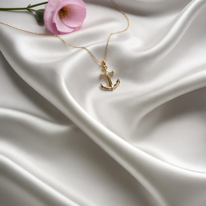 Gold anchor necklace with centre stone arranged on white silk beside a pink tulip