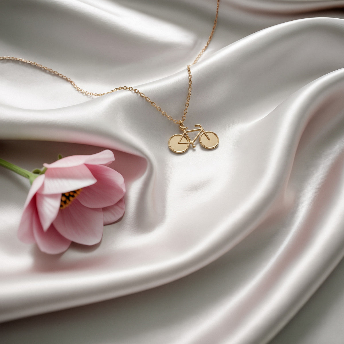 Bicycle necklace on white silk beside a pink tulip, wheels and frame in full view
