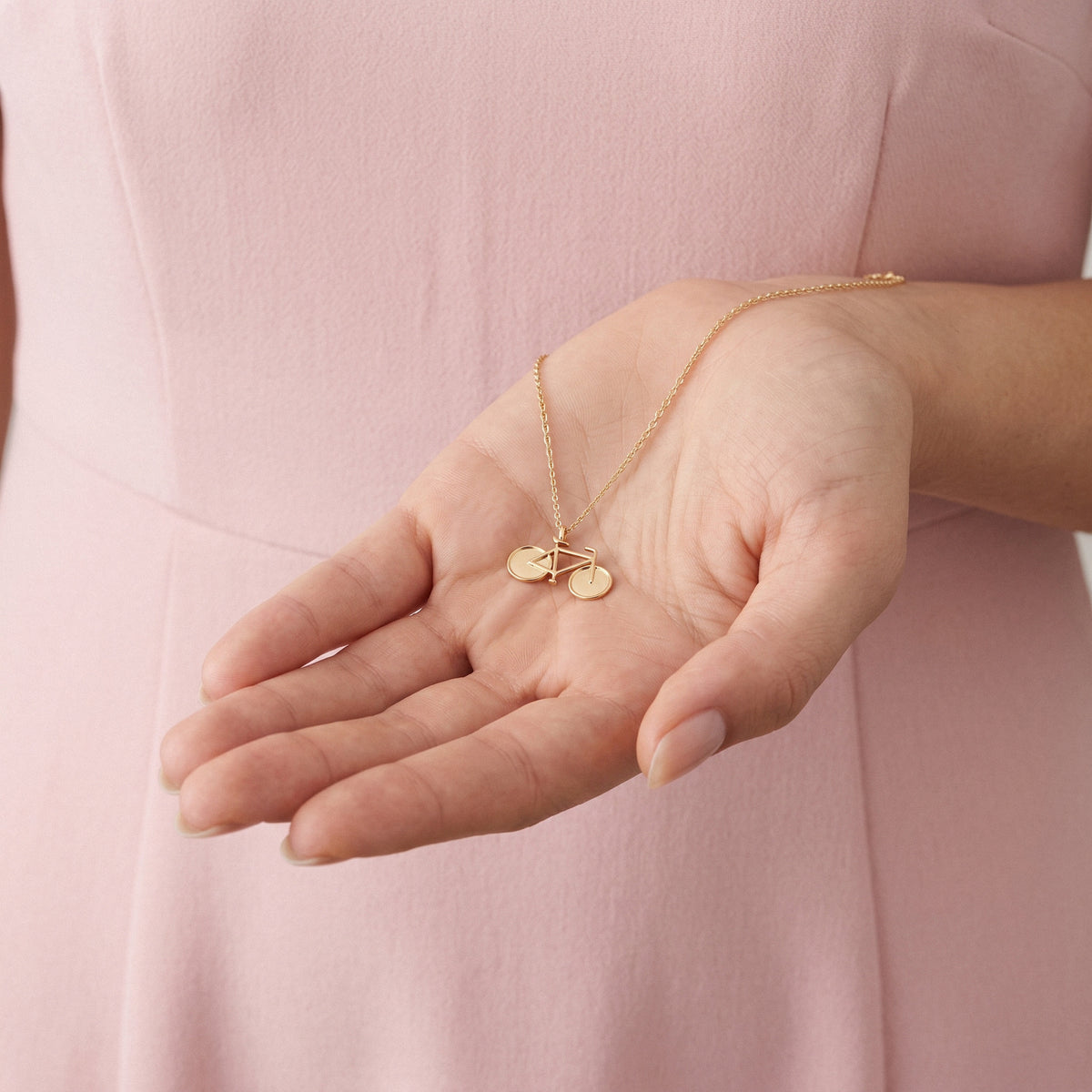 Small gold bicycle pendant resting in an open palm