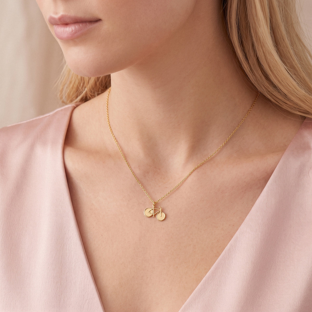 Gold bicycle necklace worn with a pink wrap top, pendant lying flat at the collarbone