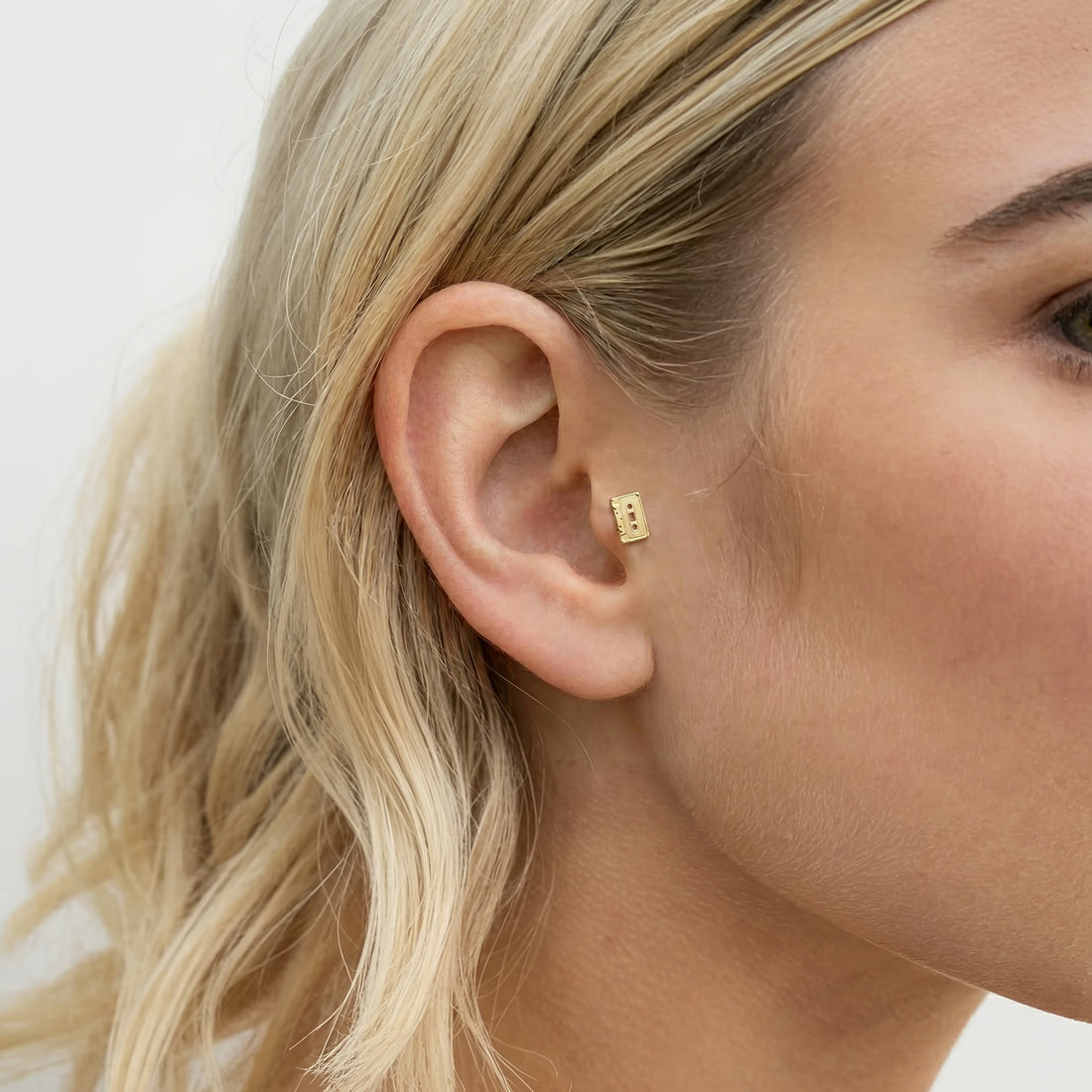 Ear close-up shows the retro cassette piercing sized as a compact music-themed accent for daily wear.