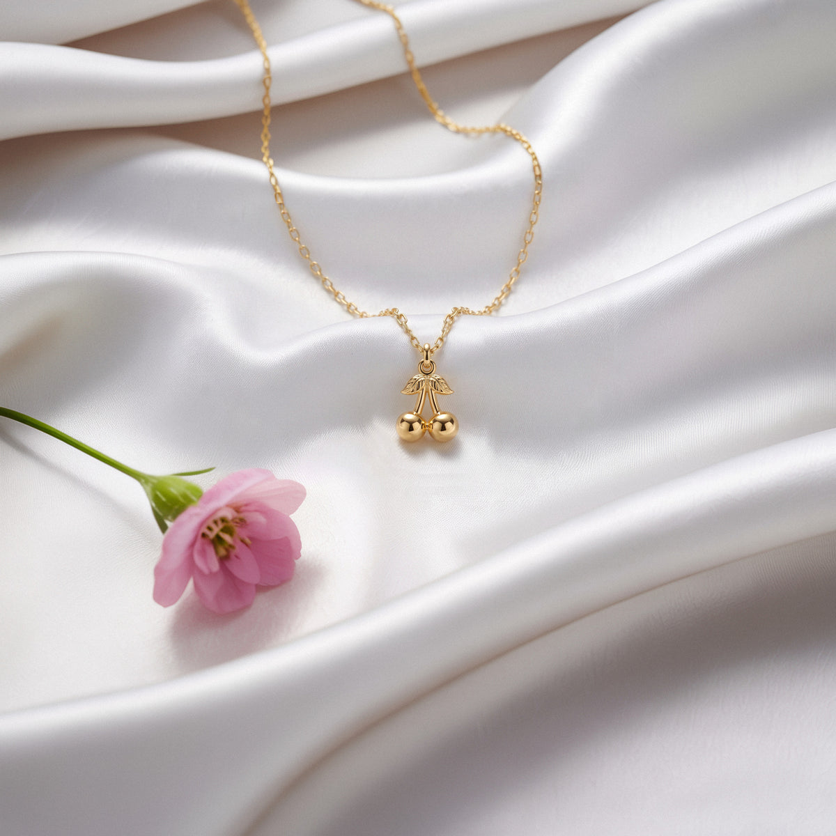 Gold cherry pendant arranged on ivory silk with a pink tulip stem crossing the frame