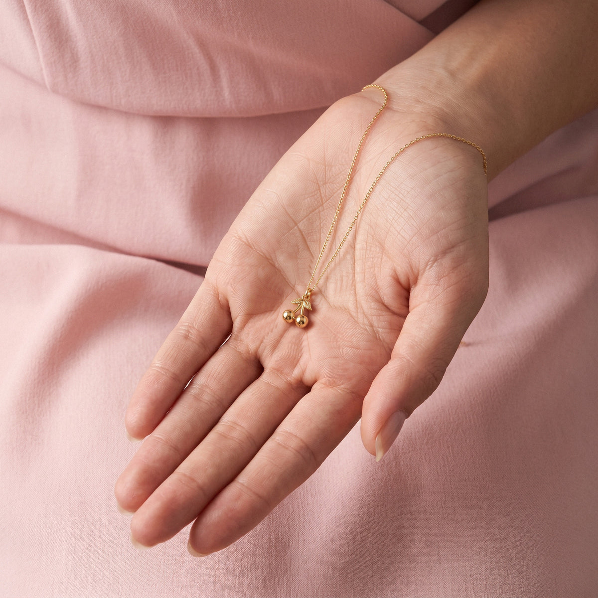 Pair of gold cherries cupped in an open hand against a dusty pink sleeve