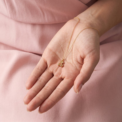 Pair of gold cherries cupped in an open hand against a dusty pink sleeve