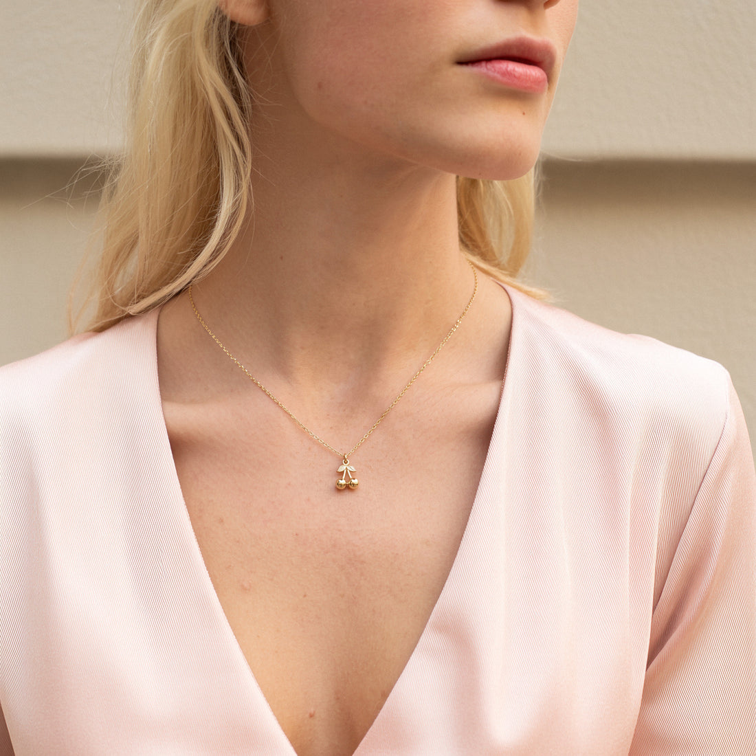 Model in a deep pink V-neck wearing the gold cherry charm at the centre of the neckline