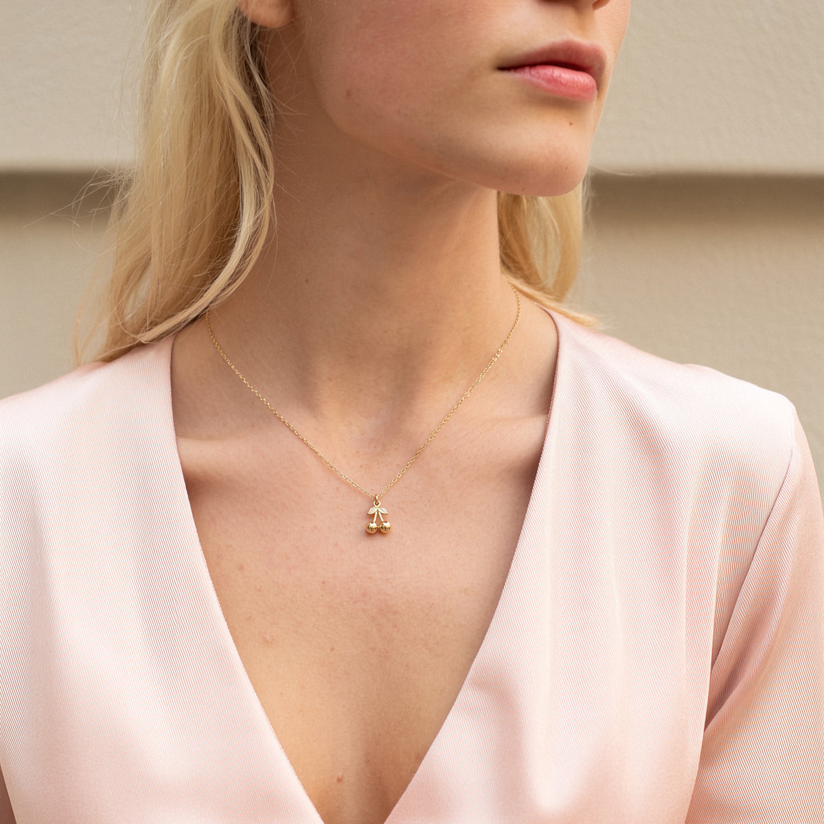 Model in a deep pink V-neck wearing the gold cherry charm at the centre of the neckline