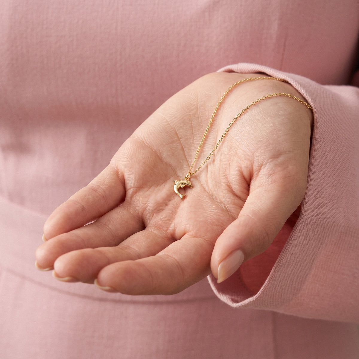 Small gold dolphin held in an open palm, chain draped over the fingers
