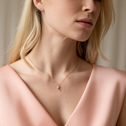 Gold dolphin charm resting just below the collarbone of a model in a soft pink top