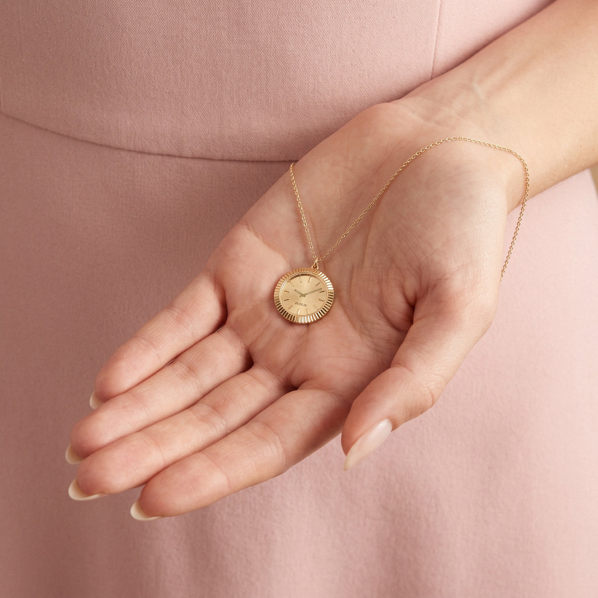 Gold watch face pendant cupped in a palm, showing the fluted edge and engraved dial