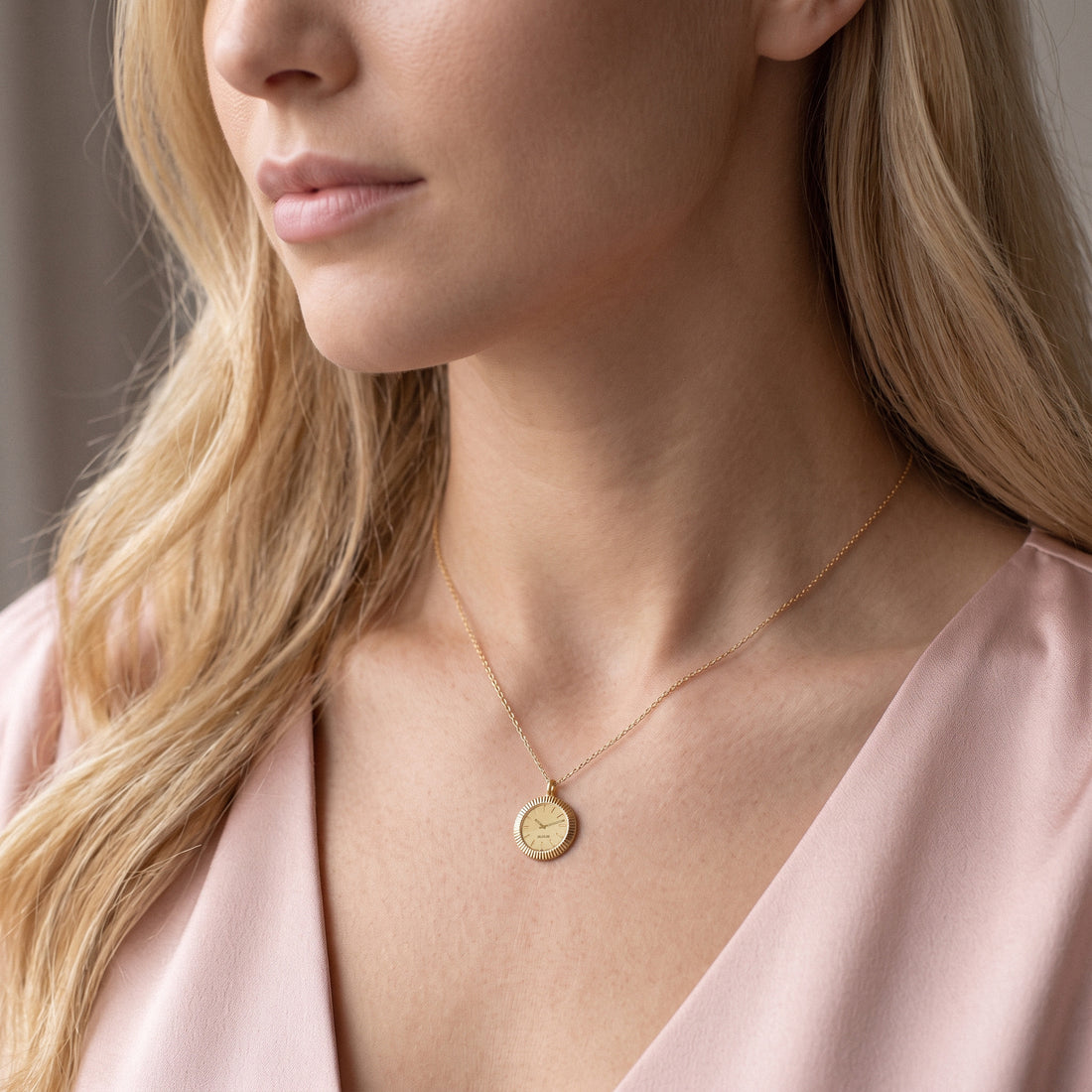 Model in a pink wrap top wearing the engraved watch face necklace