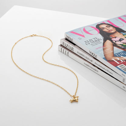 Dachshund necklace styled on a white tabletop next to a stack of fashion magazines