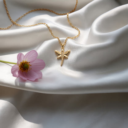 Dragonfly necklace laid over rippled white silk beside a lilac-pink cosmos