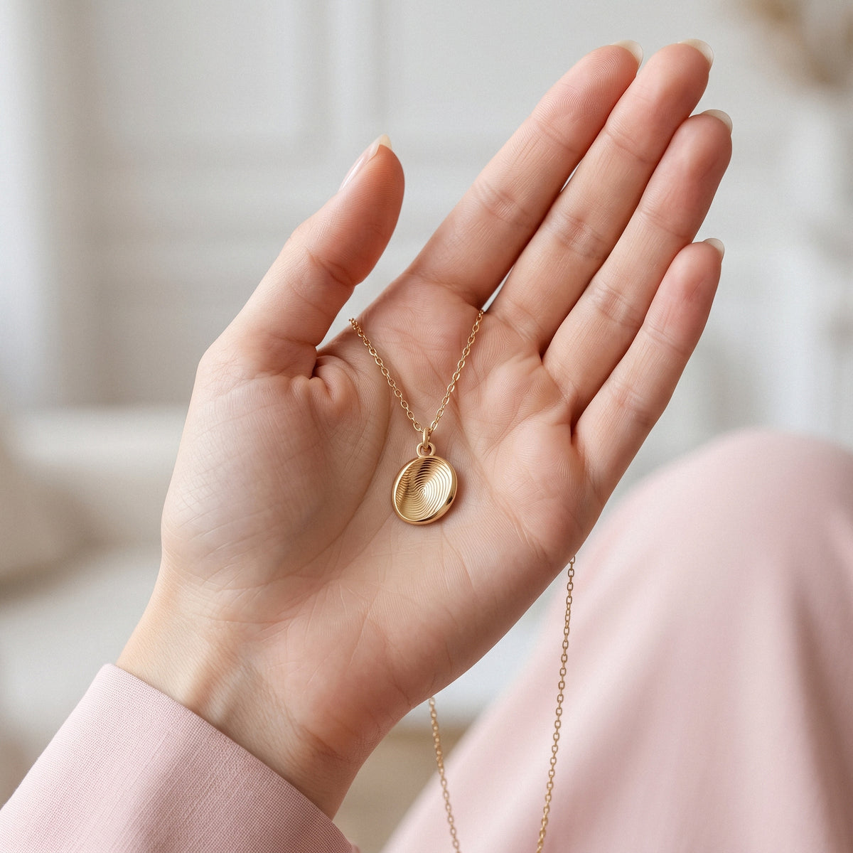 Oval fingerprint pendant held between open fingers to show its domed surface