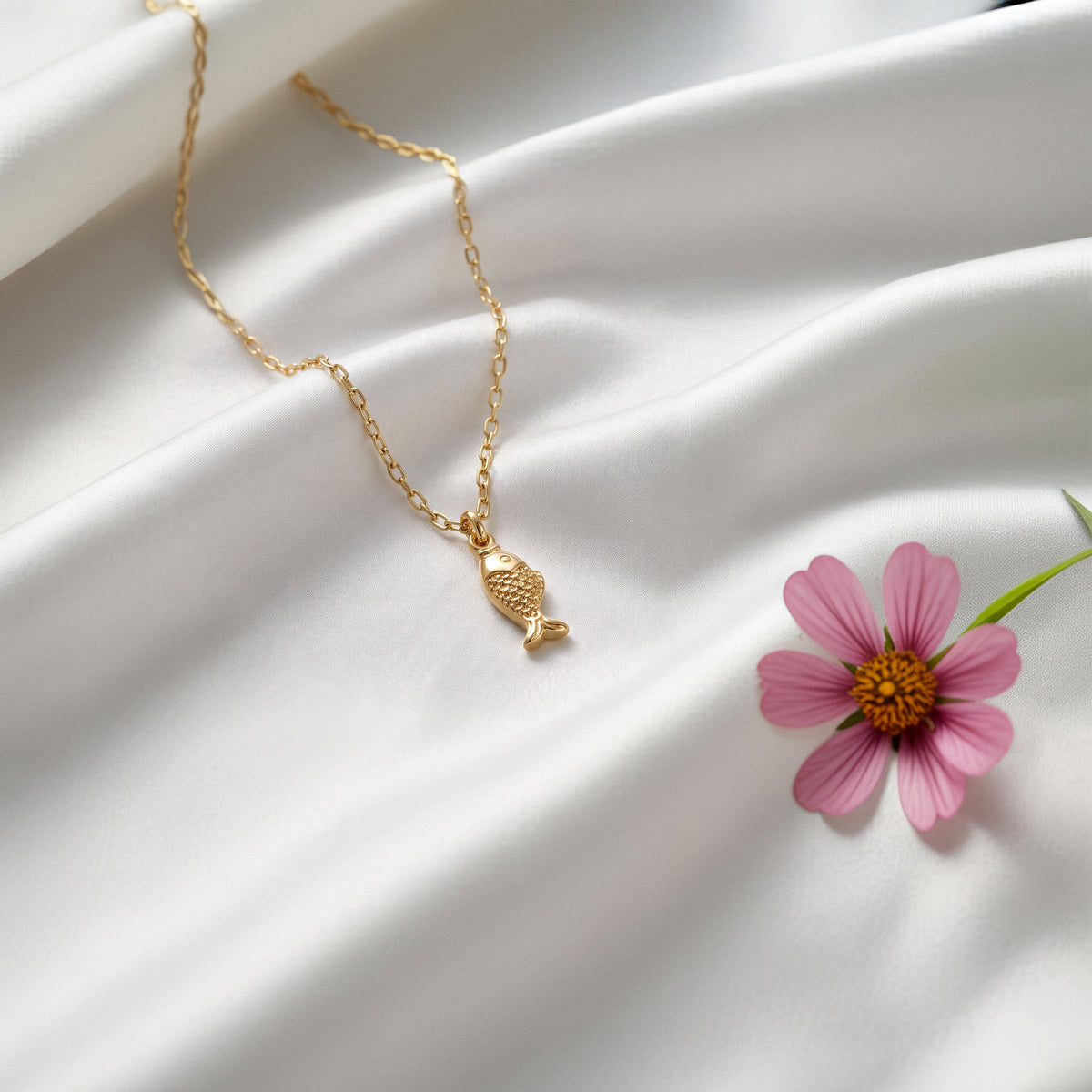 Fish pendant on white silk next to a bright pink cosmos in bloom