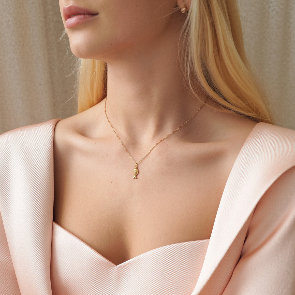 Gold fish charm worn with a pink off-shoulder top, pendant centred at the collarbone