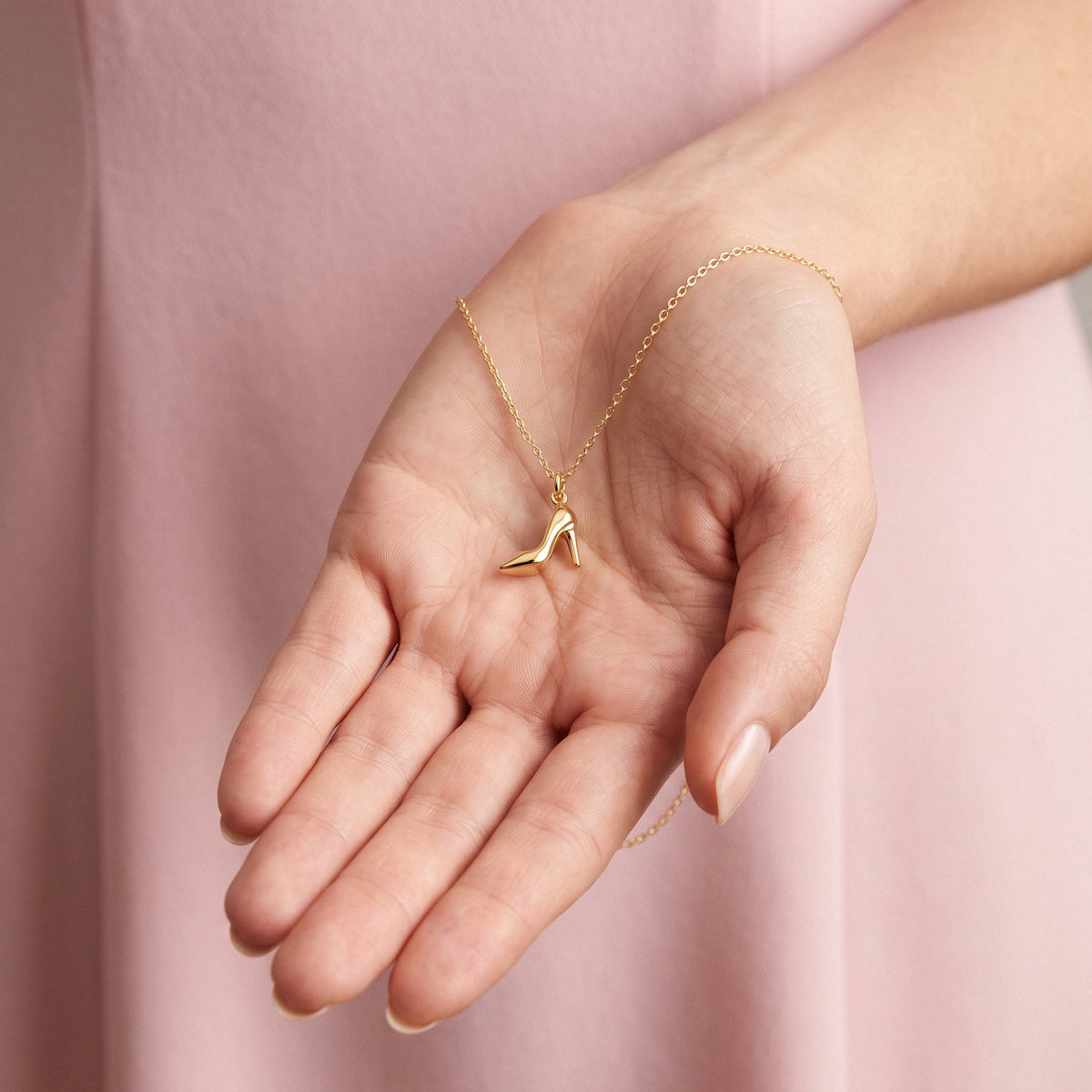 Gold stiletto charm resting in an open hand, heel pointing towards the fingers