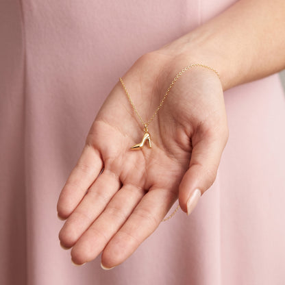 Gold stiletto charm resting in an open hand, heel pointing towards the fingers