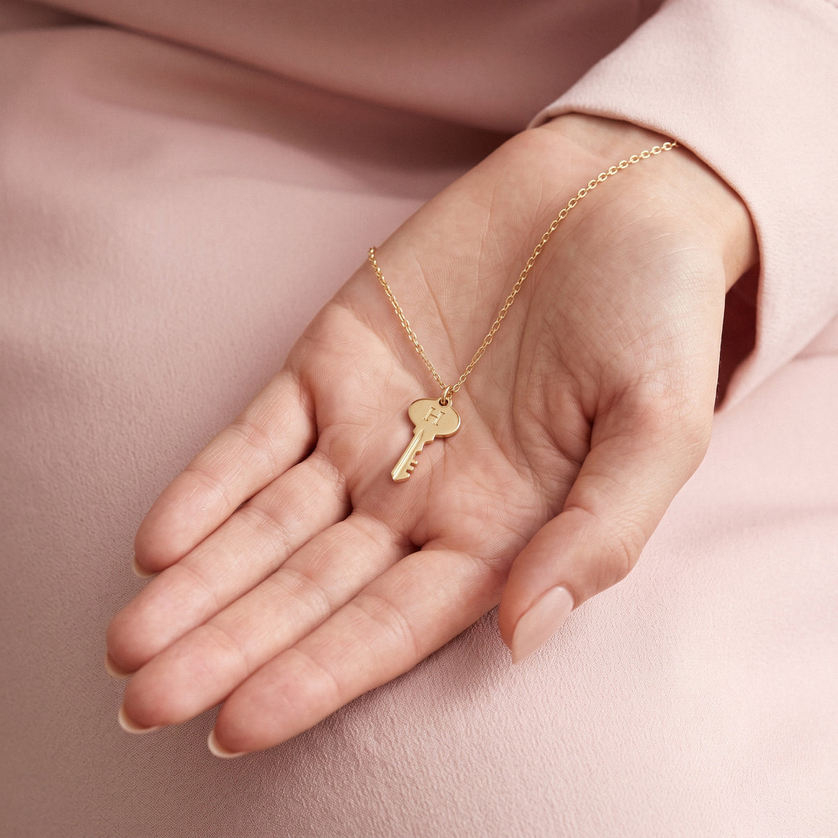 Gold key initial pendant resting in an open palm, showing how small the charm is