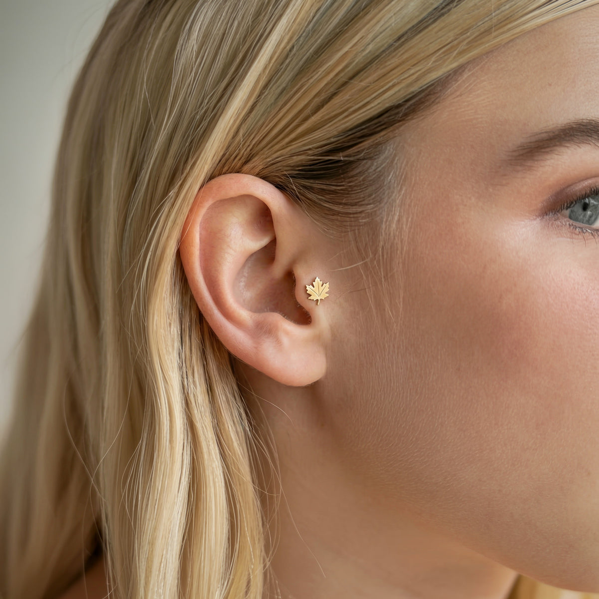 Close-up placement shows the maple leaf piercing nestled neatly against the ear in a nature-inspired stack.