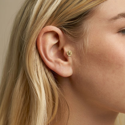 Close ear view of the Medusa portrait flatback piercing, revealing its compact mythological profile in a curated stack.