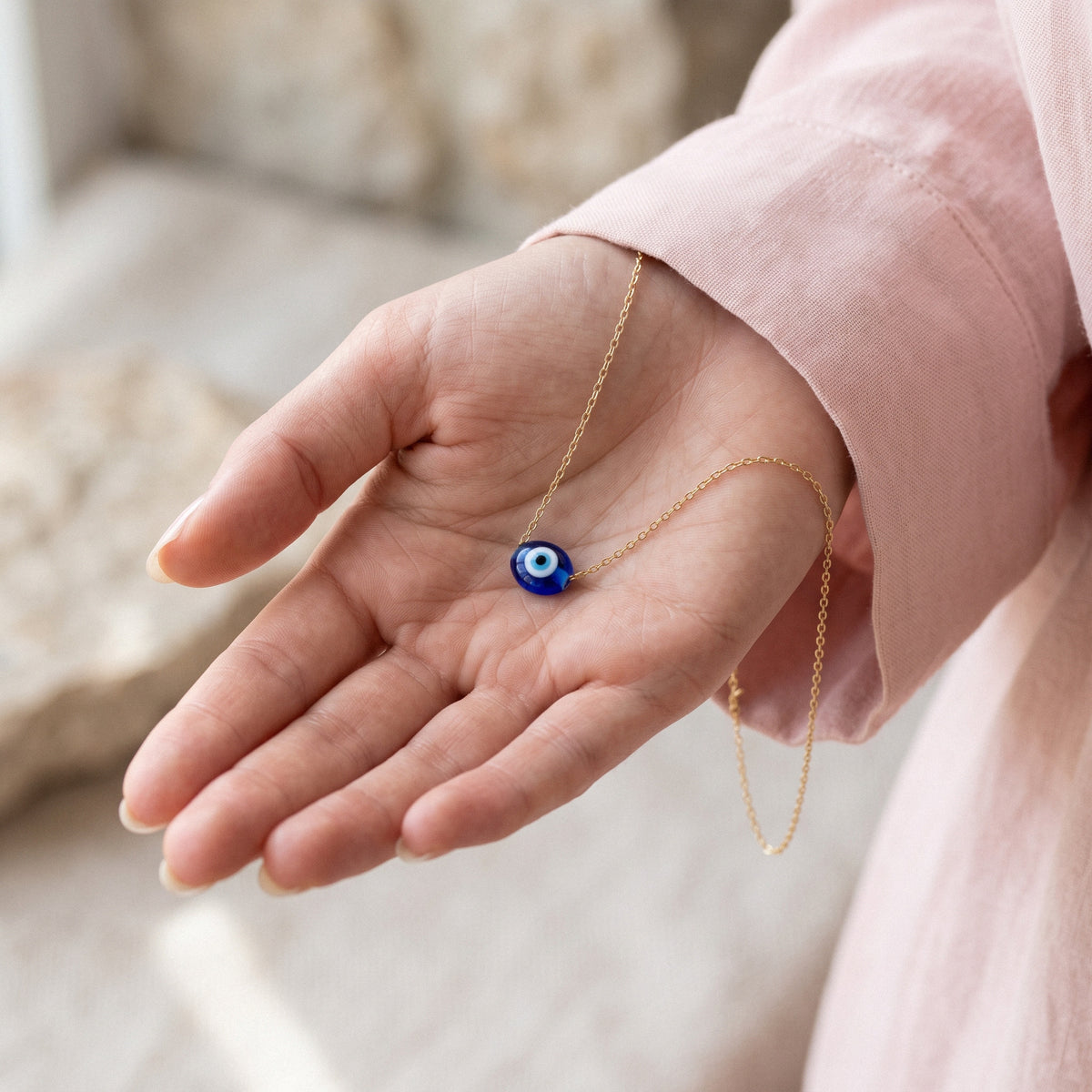 Blue oval charm resting in an outstretched hand outdoors, chain falling from the wrist