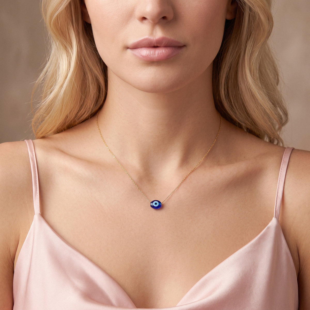 Oval blue evil eye centred above a blush satin camisole in a front model portrait