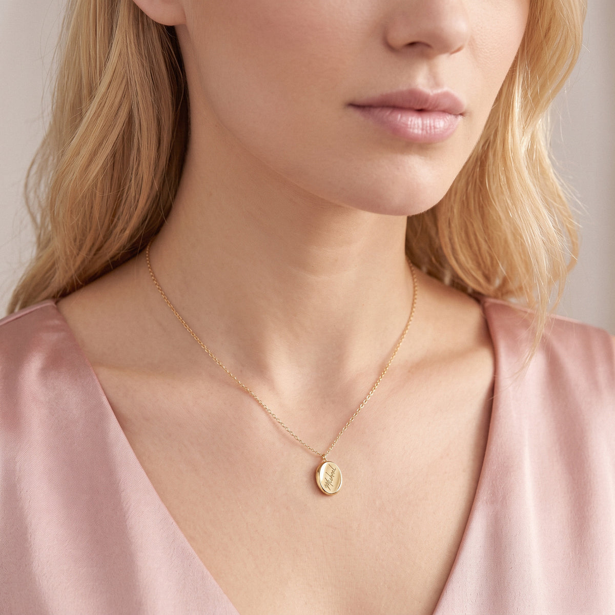 Script name engraving seen close on the gold oval pendant