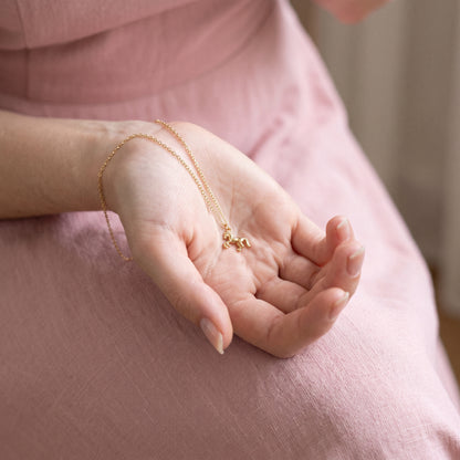 Gold horse displayed in a gently cupped hand, the chain trailing across a pink skirt