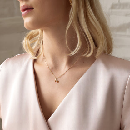 Small horse charm worn above a pale pink wrap neckline on a model with a blonde bob