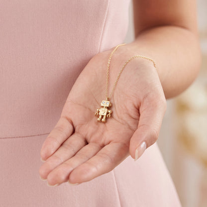 Robot charm lying on the palm of a hand against a pink dress, arms and legs clearly visible