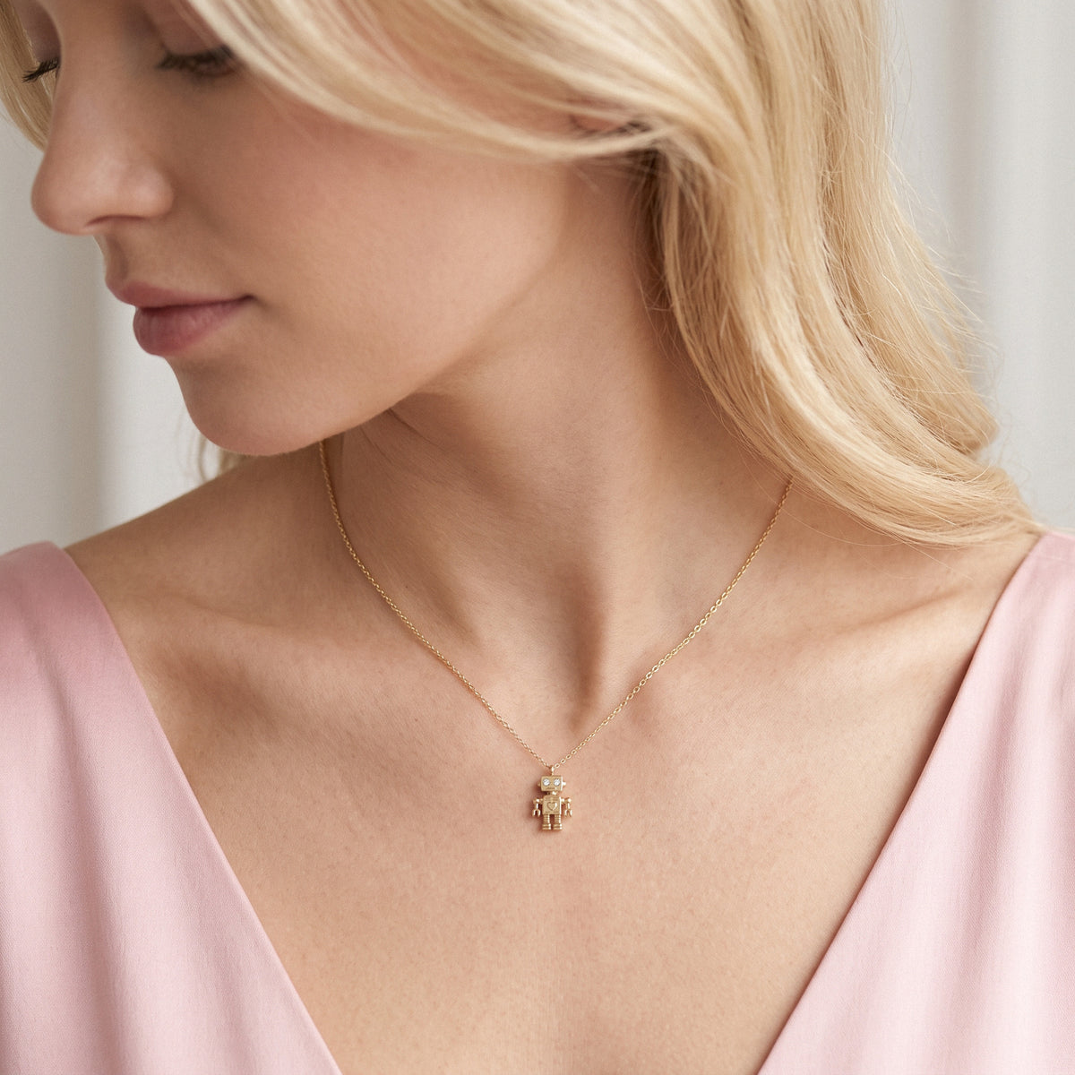 Model in a pink v-neck wearing the gold robot necklace, charm detail in focus