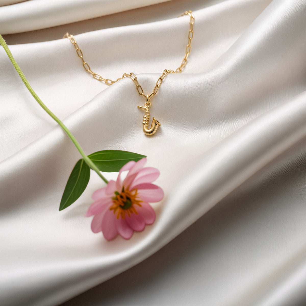 Tiny saxophone arranged on luminous white silk with a pink cosmos and green stem
