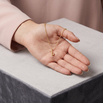 Musical pendant held over a grey velvet block, chain circling the model&