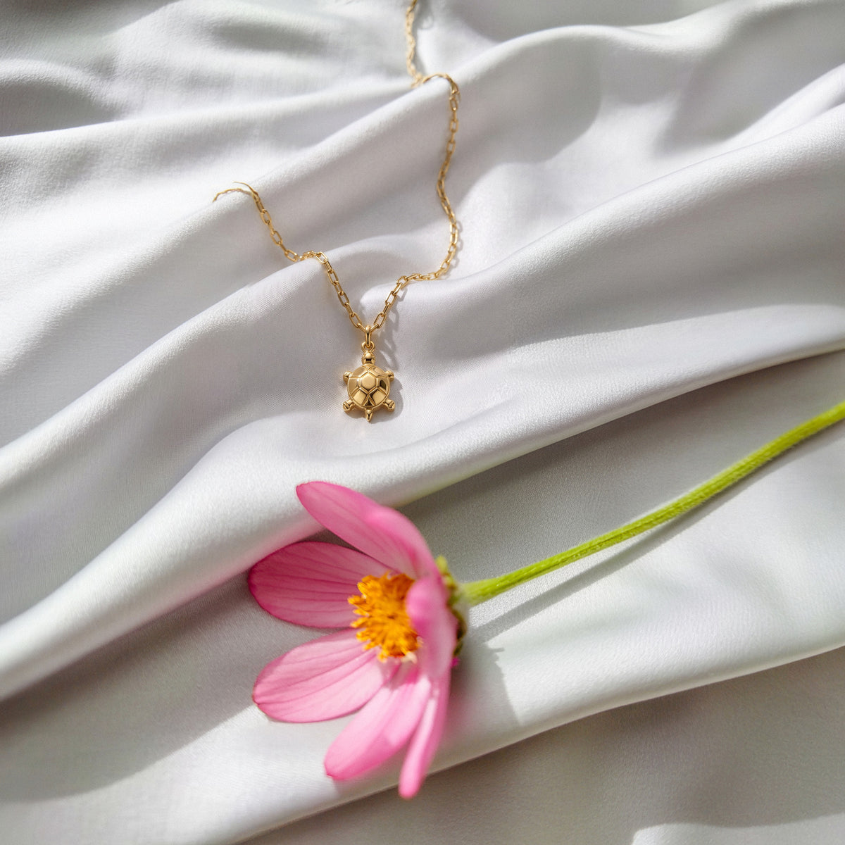 Turtle pendant on white silk, a pink cosmos lying across the fabric